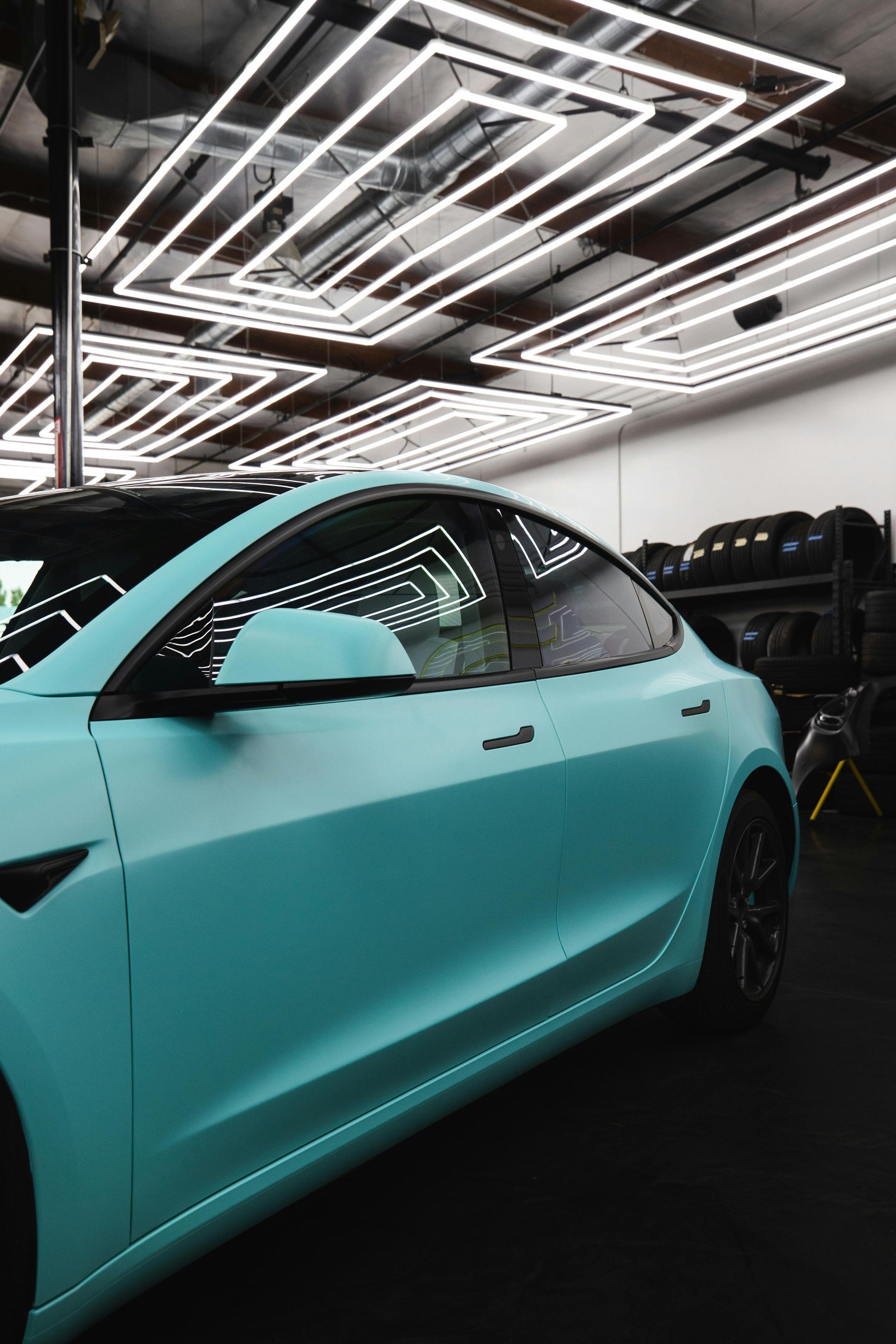 Aqua-colored Tesla sedan parked inside a garage, bright overhead lighting.