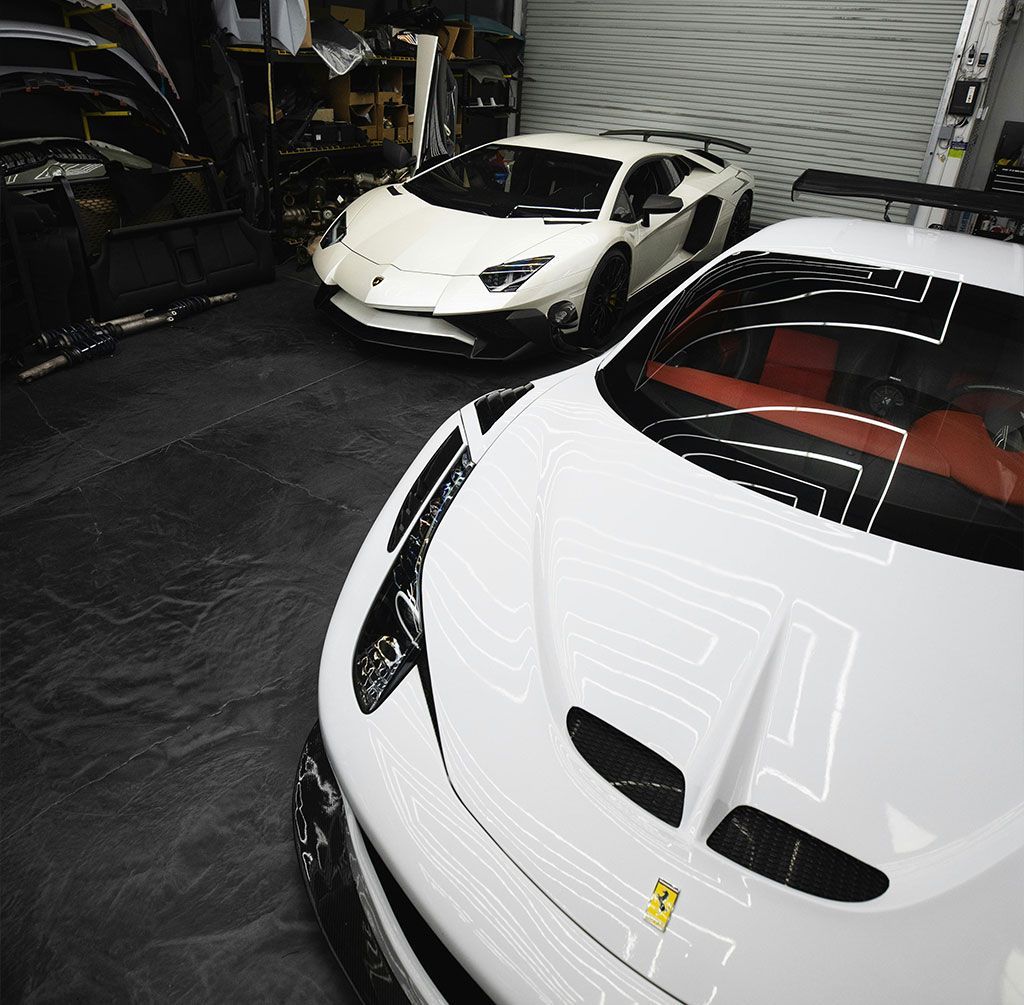 White Lamborghini and Ferrari parked in a garage with accessories in the background.