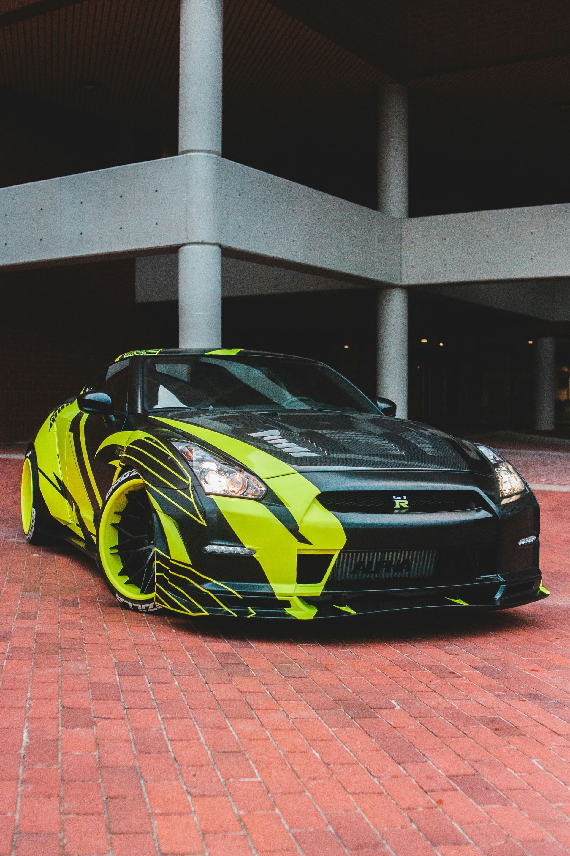 Black and neon green Nissan GT-R sports car with custom graphics, parked outdoors under a building.