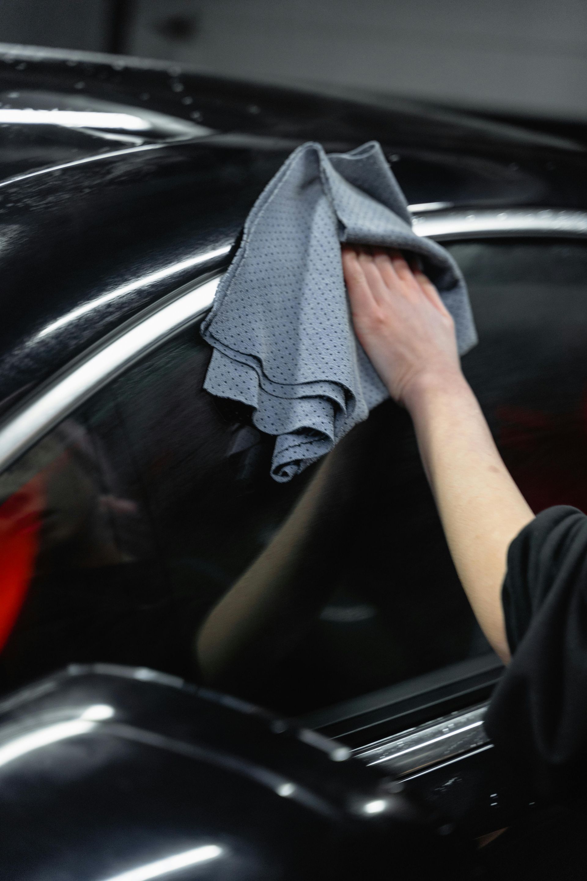 Person wiping a black car window with a gray microfiber cloth.