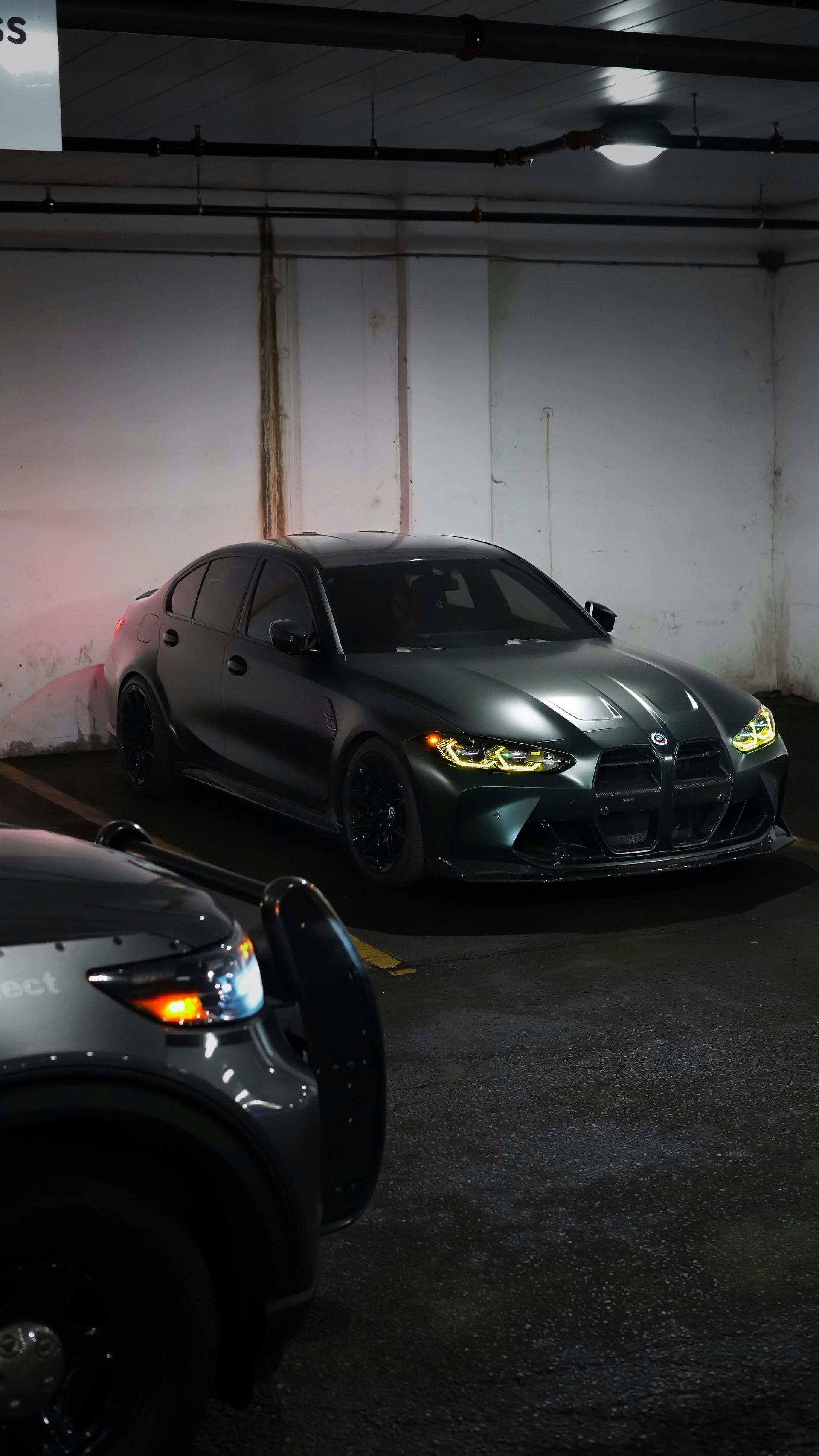Dark gray BMW sedan in a dimly lit parking garage, next to a partially visible dark-colored SUV.