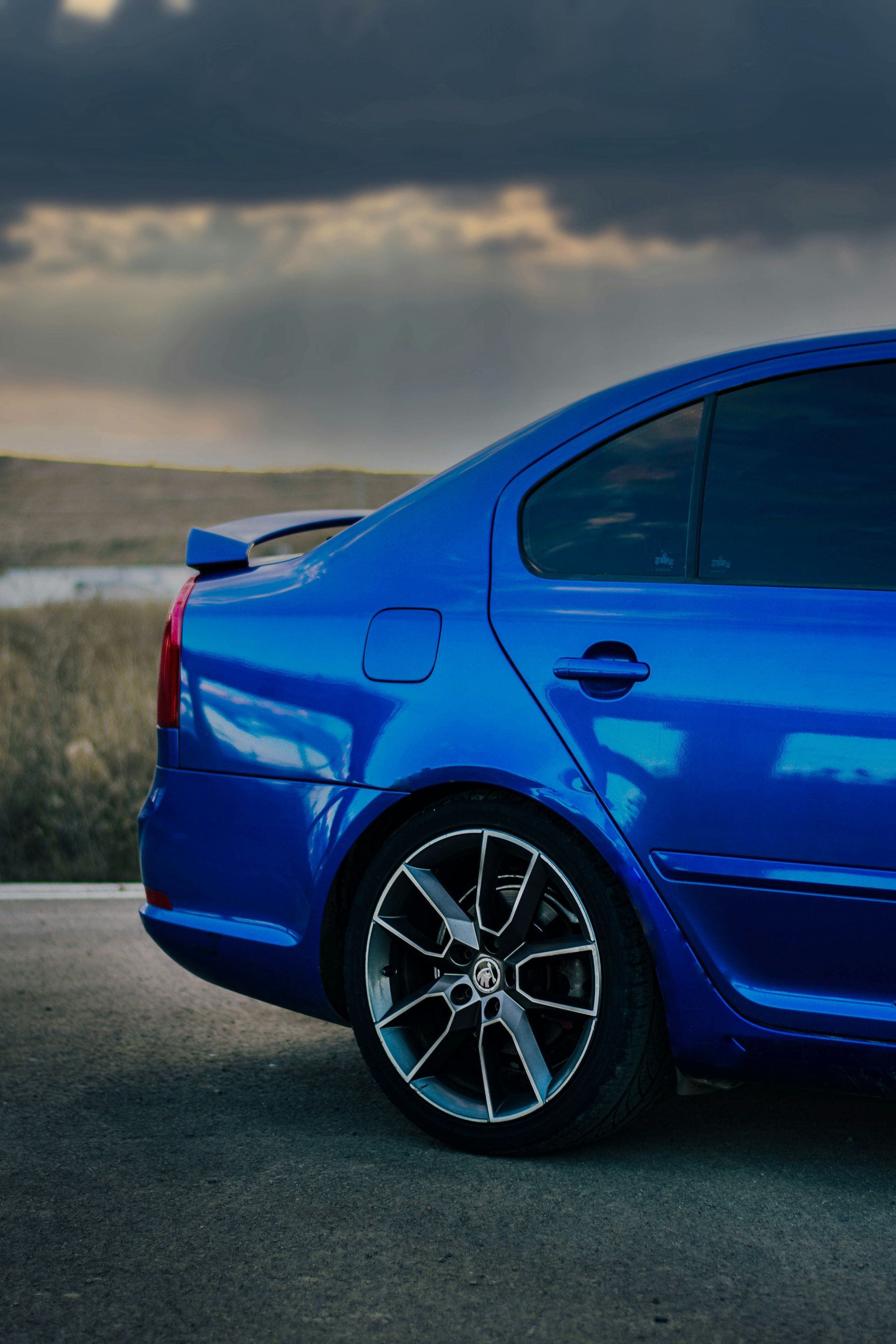 Blue car parked on asphalt road with cloudy sky in the background.