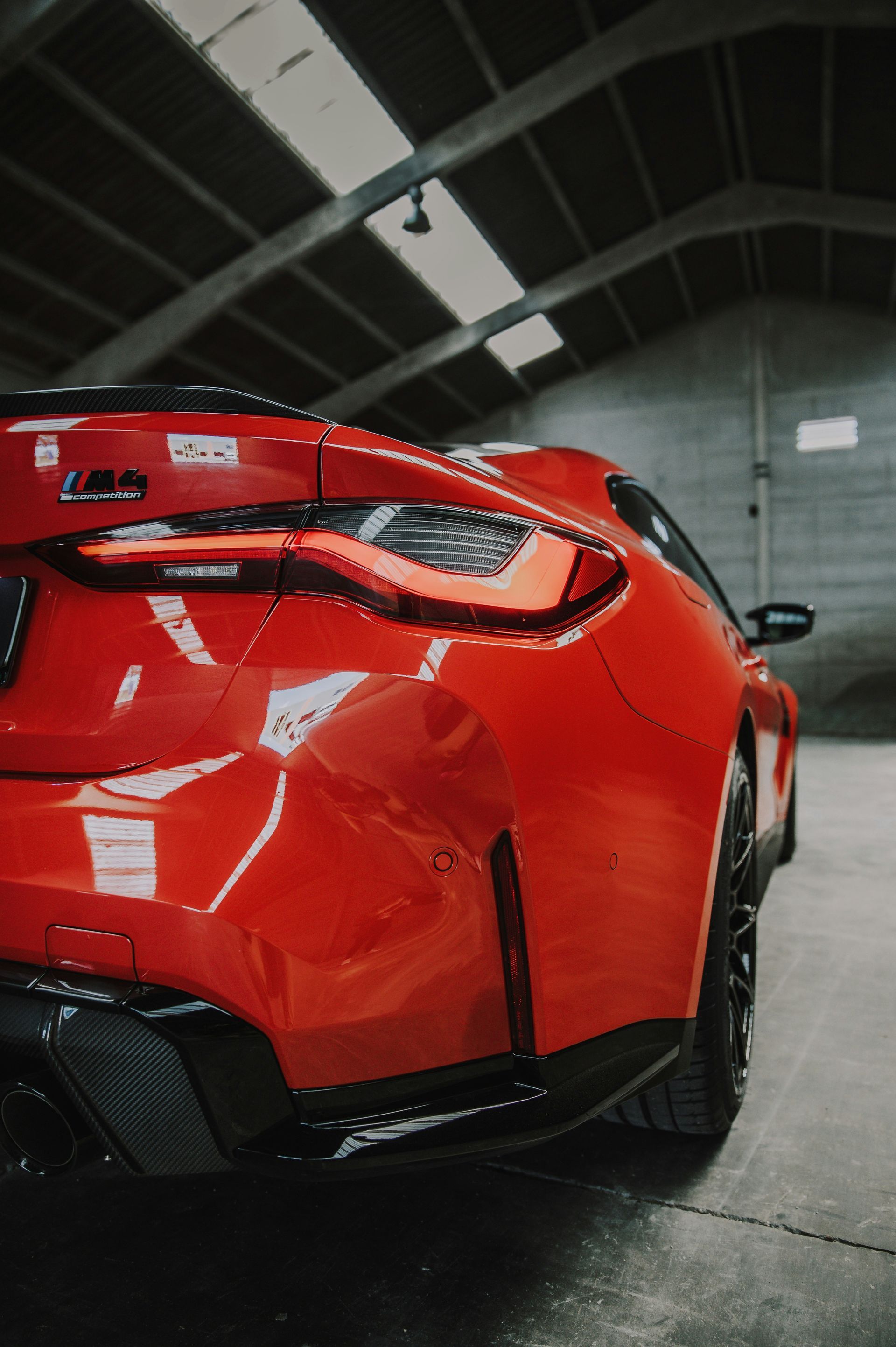 Red BMW M4 coupe parked inside a garage, showcasing its rear end.