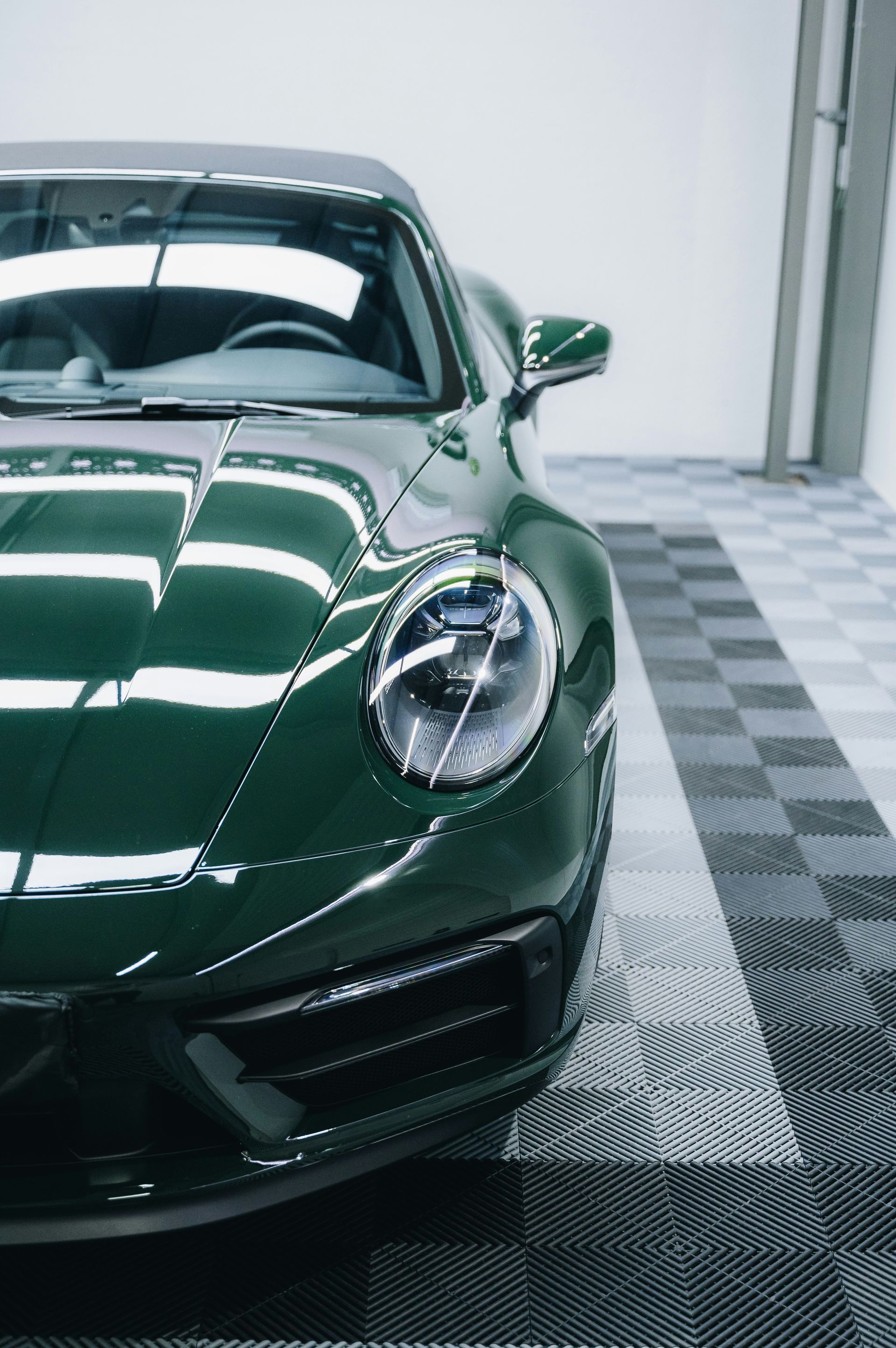 Green Porsche sports car, front quarter view, in a garage with checkered floor.
