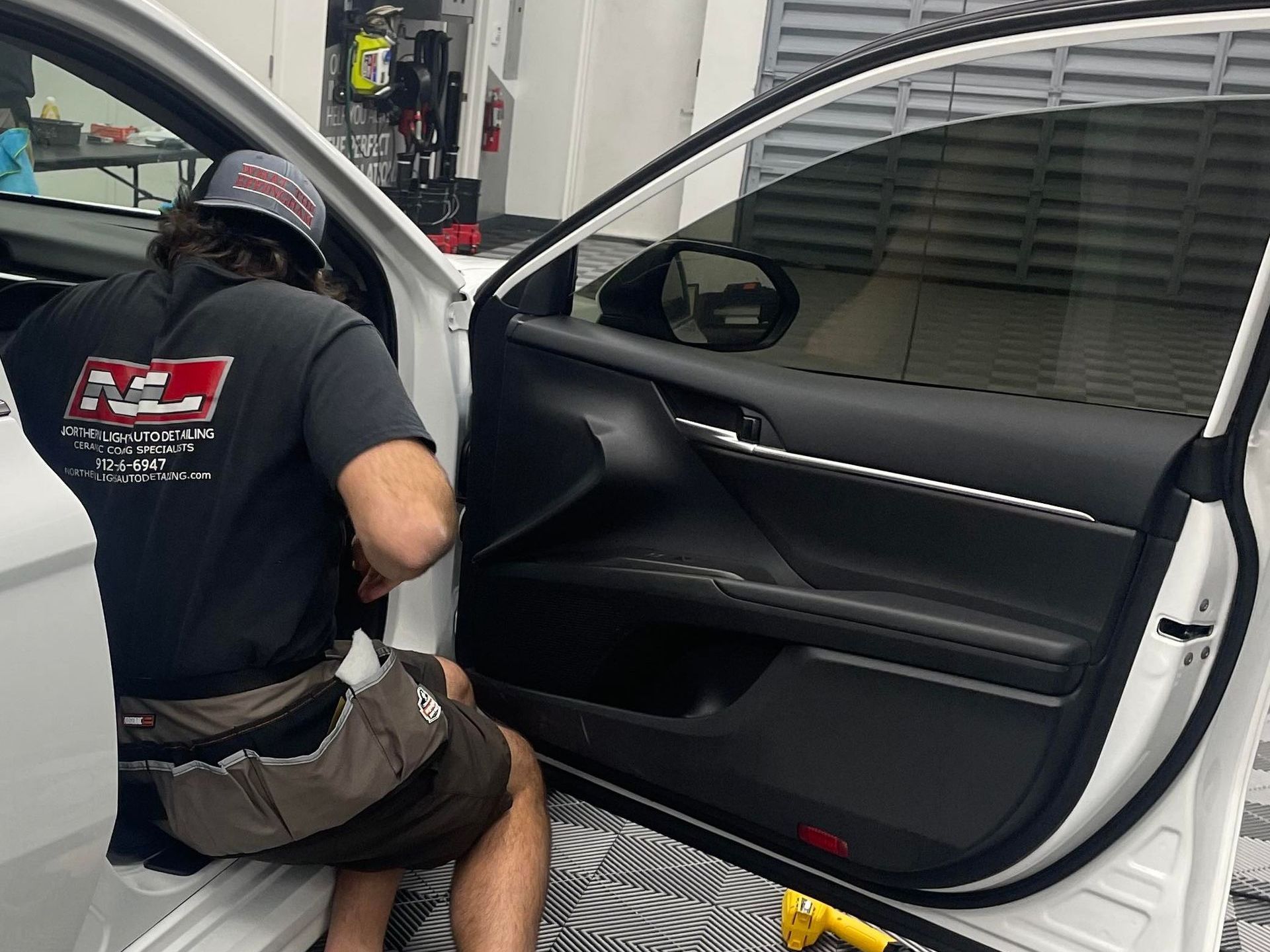 A man in a black shirt is kneeling in a white car.