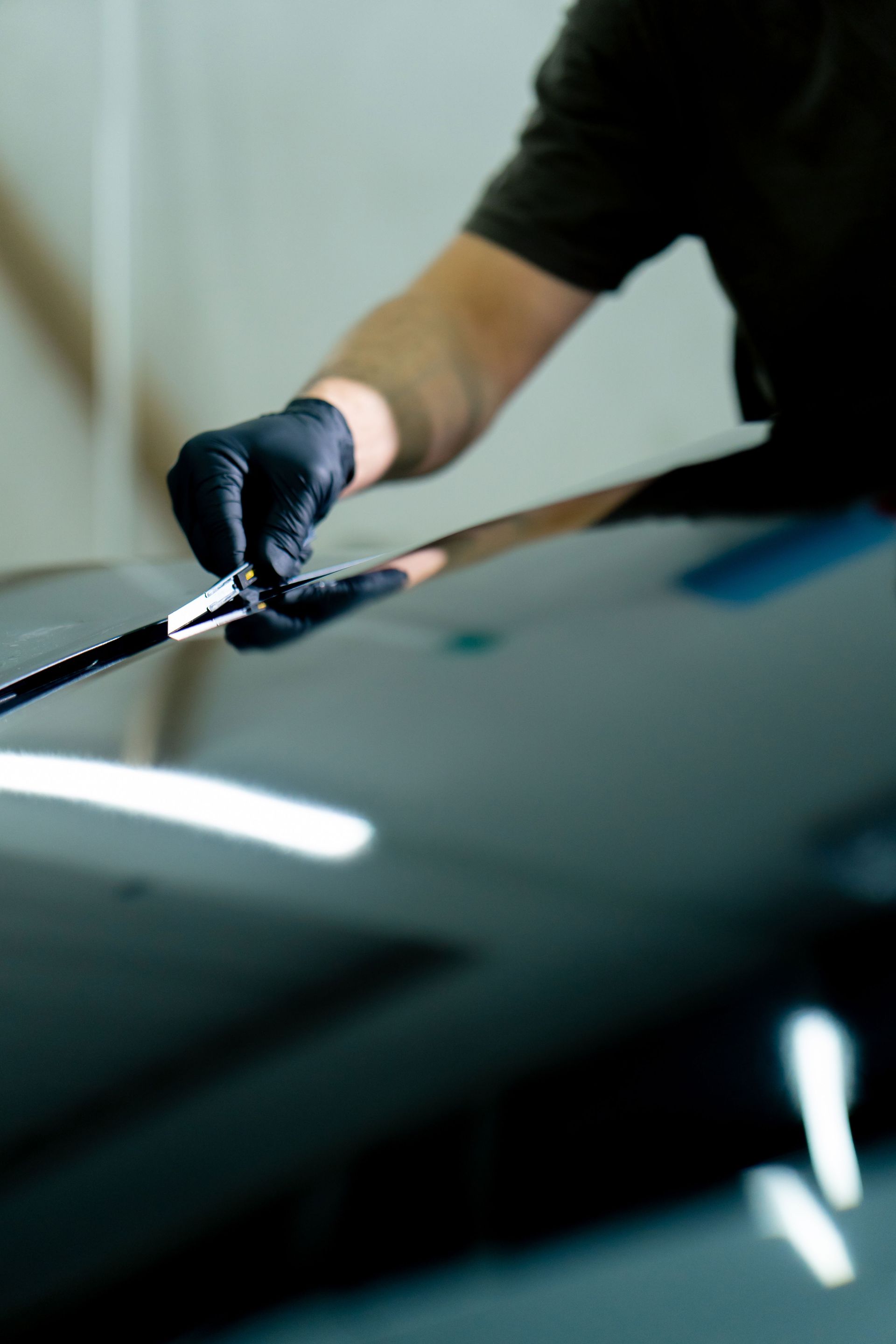 Person wearing black gloves applying coating to a black car hood.