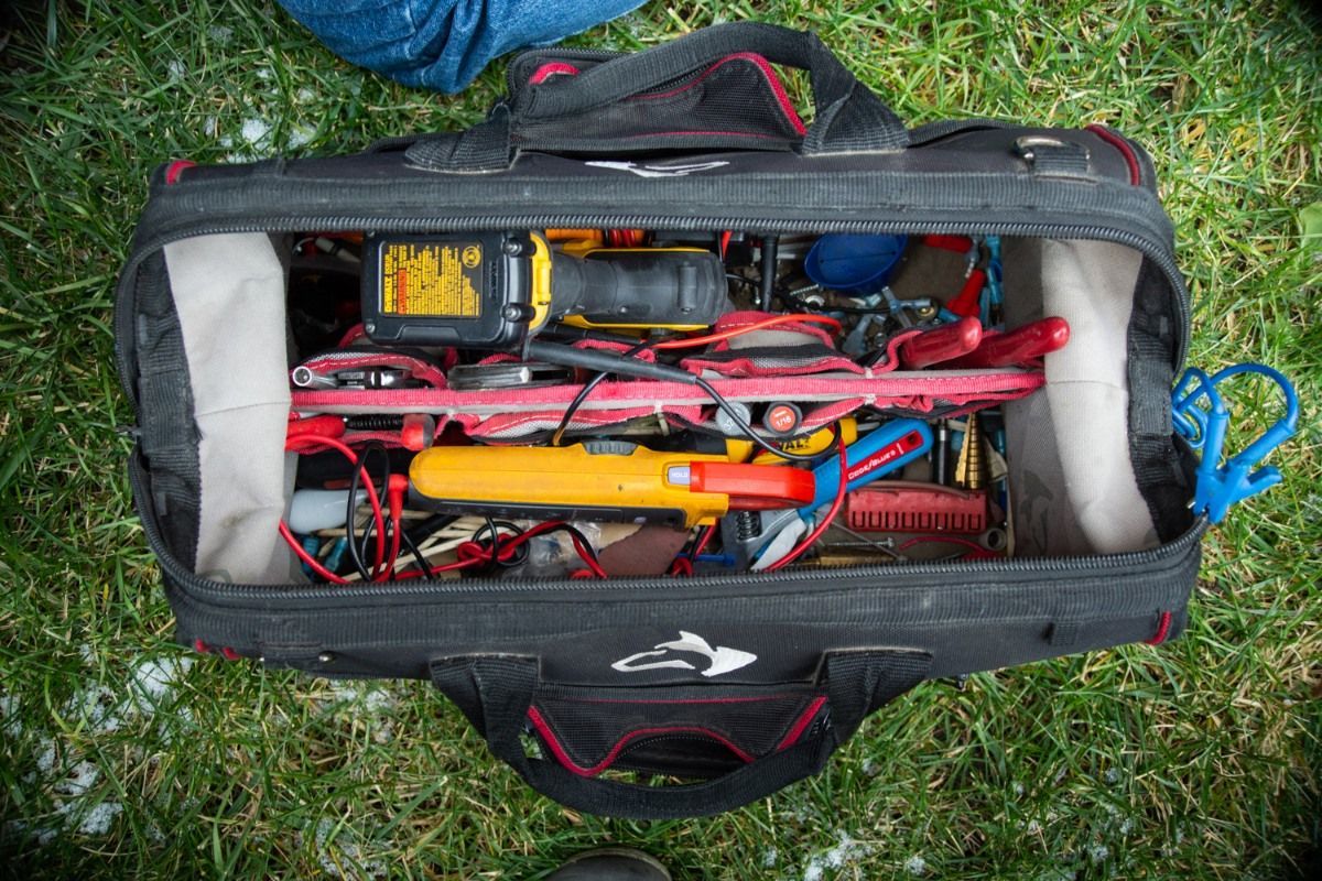 Open black tool bag on grass, filled with assorted tools: red, yellow, black.