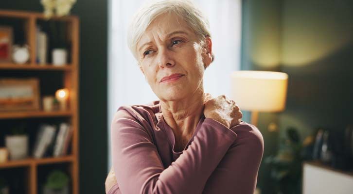 An elderly woman with short white hair, clutching her shoulder, is expressing pain. Treating Fibromyalgia with Acupuncture: Understanding A Holistic Approach