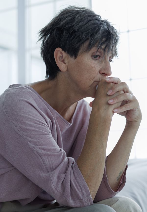 Woman with short gray hair, in a pink shirt, looks down pensively with hands clasped near her mouth.  She is sitting near a window. Acupuncture for Chronic Insomnia by Marc Bystock NYC Acupuncturist in Midtown Manhattan NY 10016