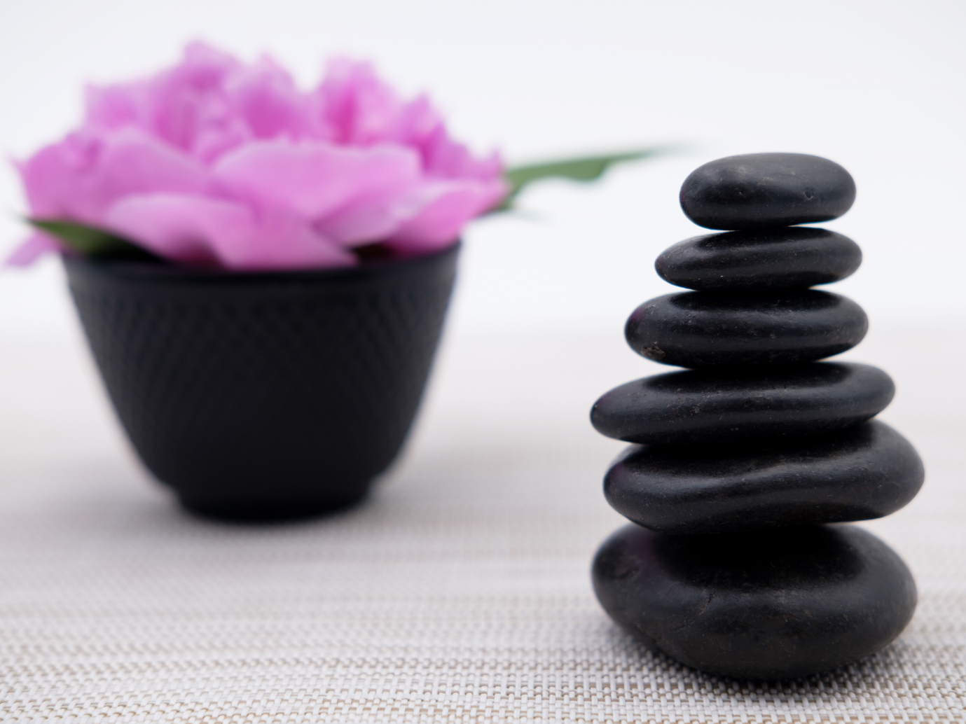 Black zen stones stacked with a pink flower in a black bowl.
