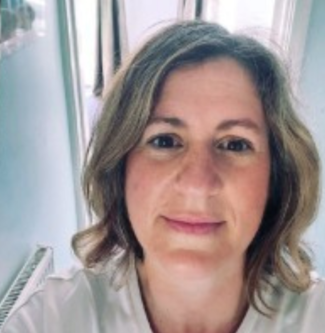 Woman with light brown hair, smiling softly at camera, indoors.