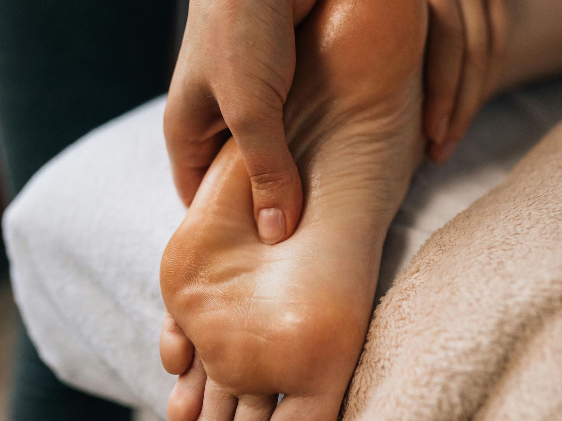 Hand massaging the sole of a foot, showing the arch and skin. The foot is on a towel.