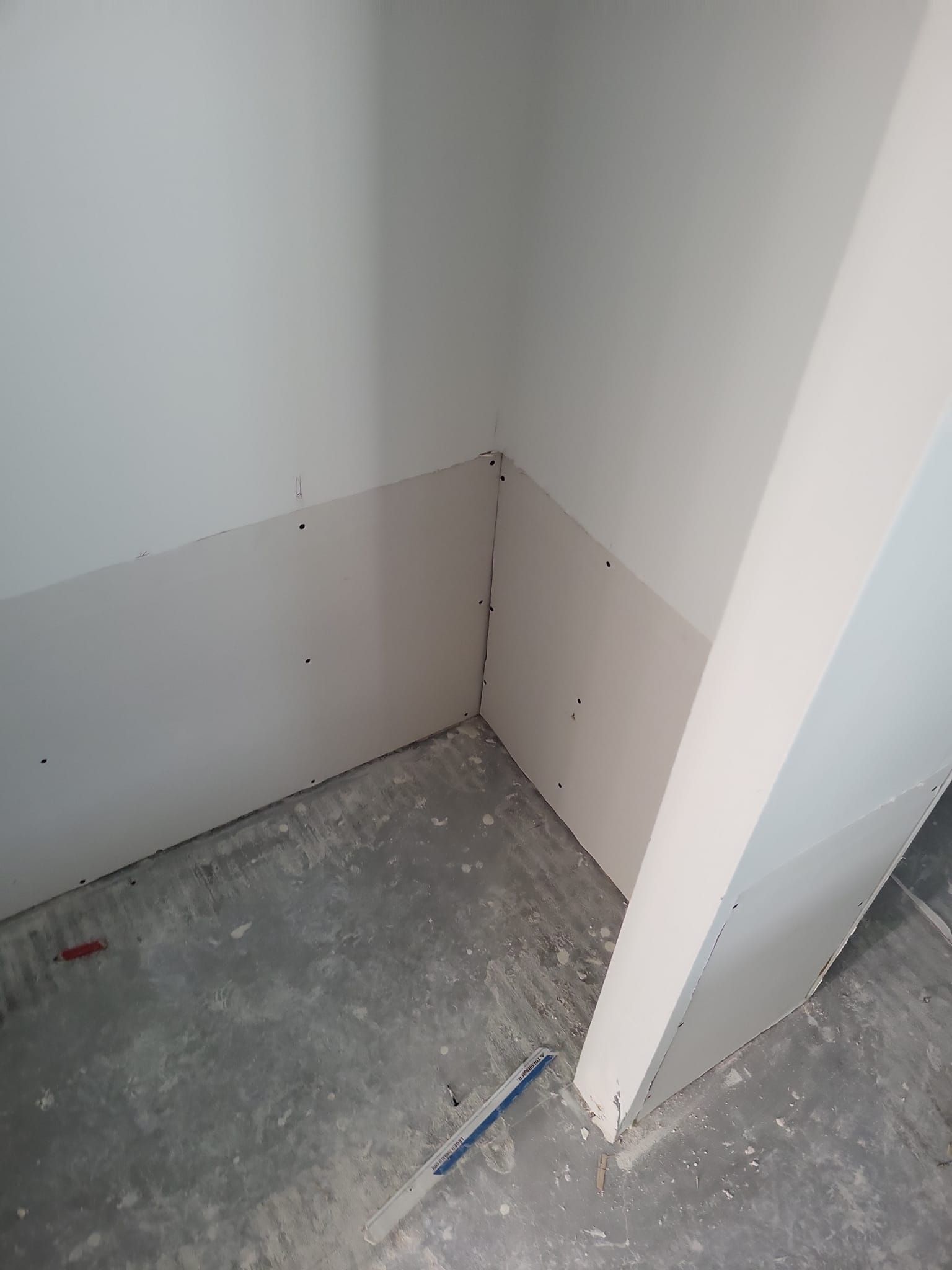 Un coin d'une pièce avec un mur blanc et une règle bleue sur le sol.