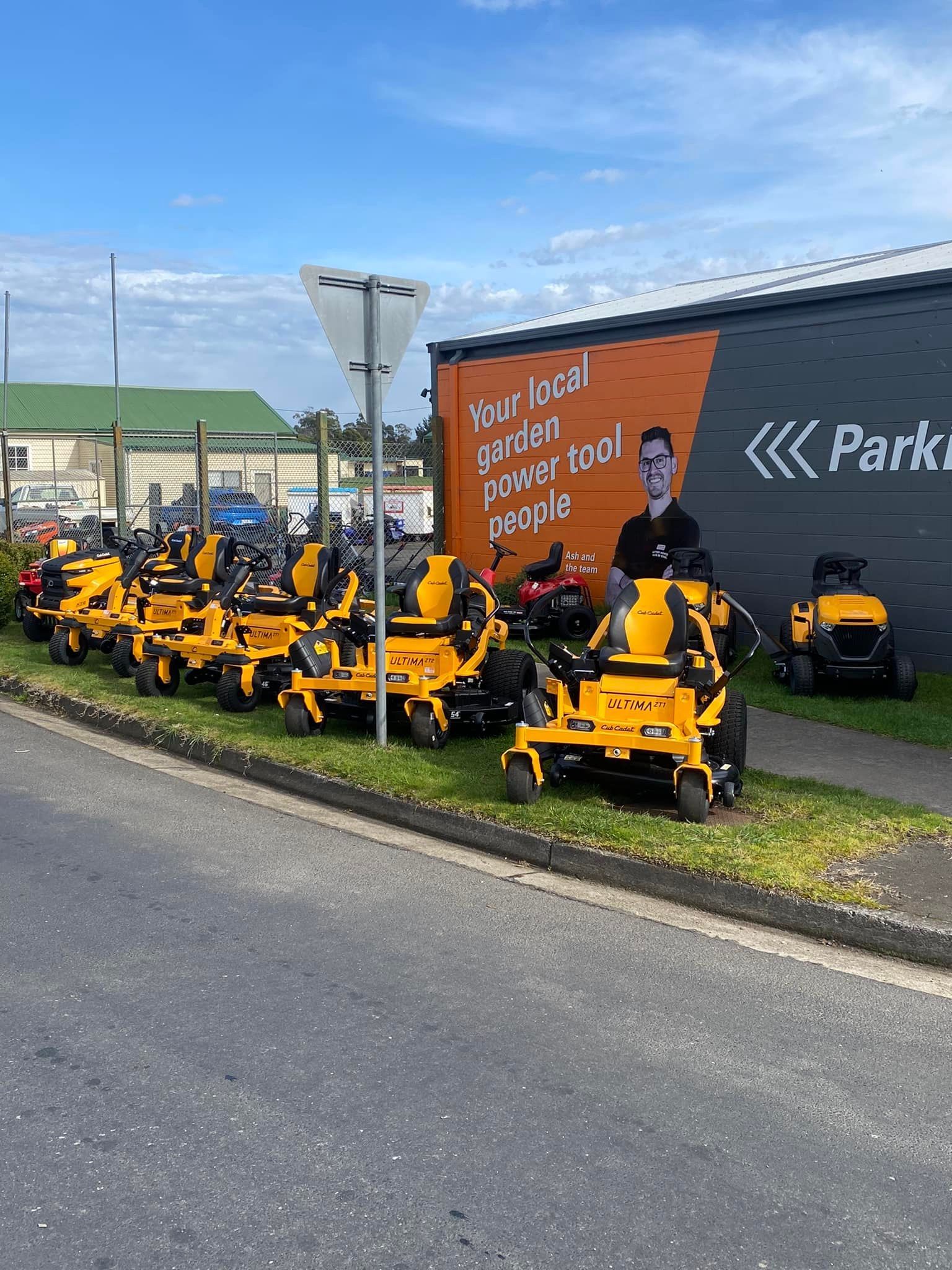 Yellow lawn mowers parked in front of a store with orange and black signage.