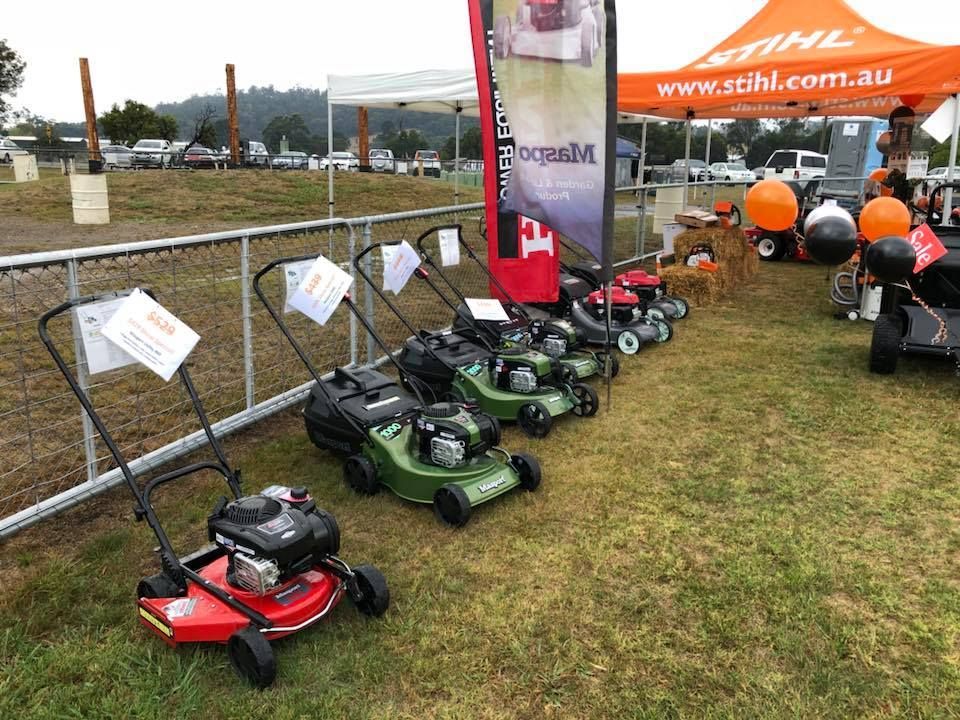 Lawnmowers on display at an outdoor event, green grass, Stihl sign, sunny setting.