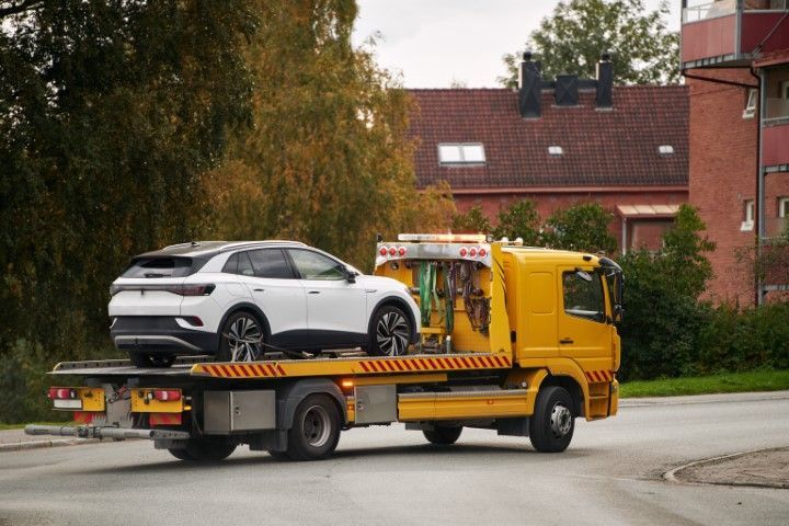 Yellow tow truck carrying a white SUV on a flatbed in a suburban street