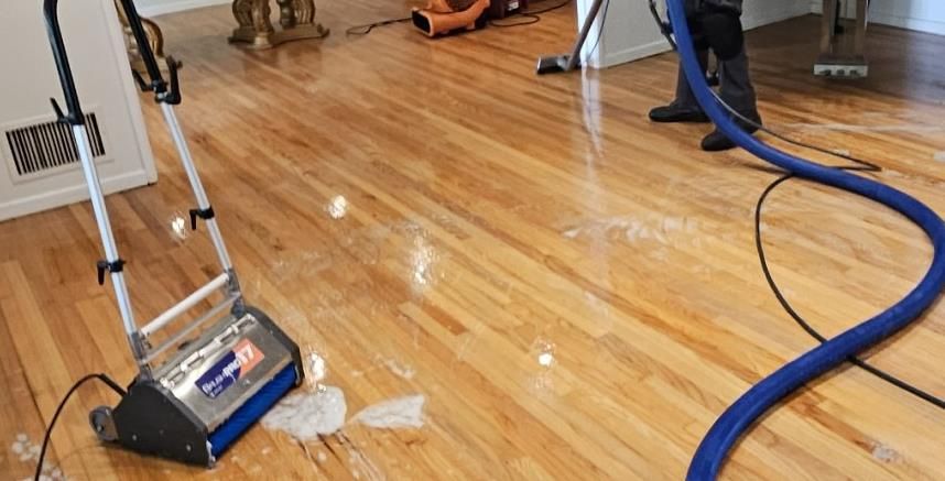 A person is cleaning a wooden floor with a vacuum cleaner.