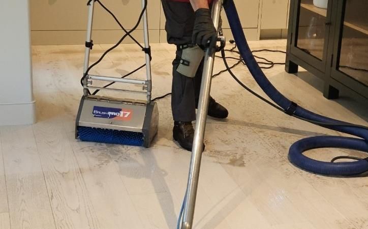 A person is cleaning a wooden floor with a vacuum cleaner.