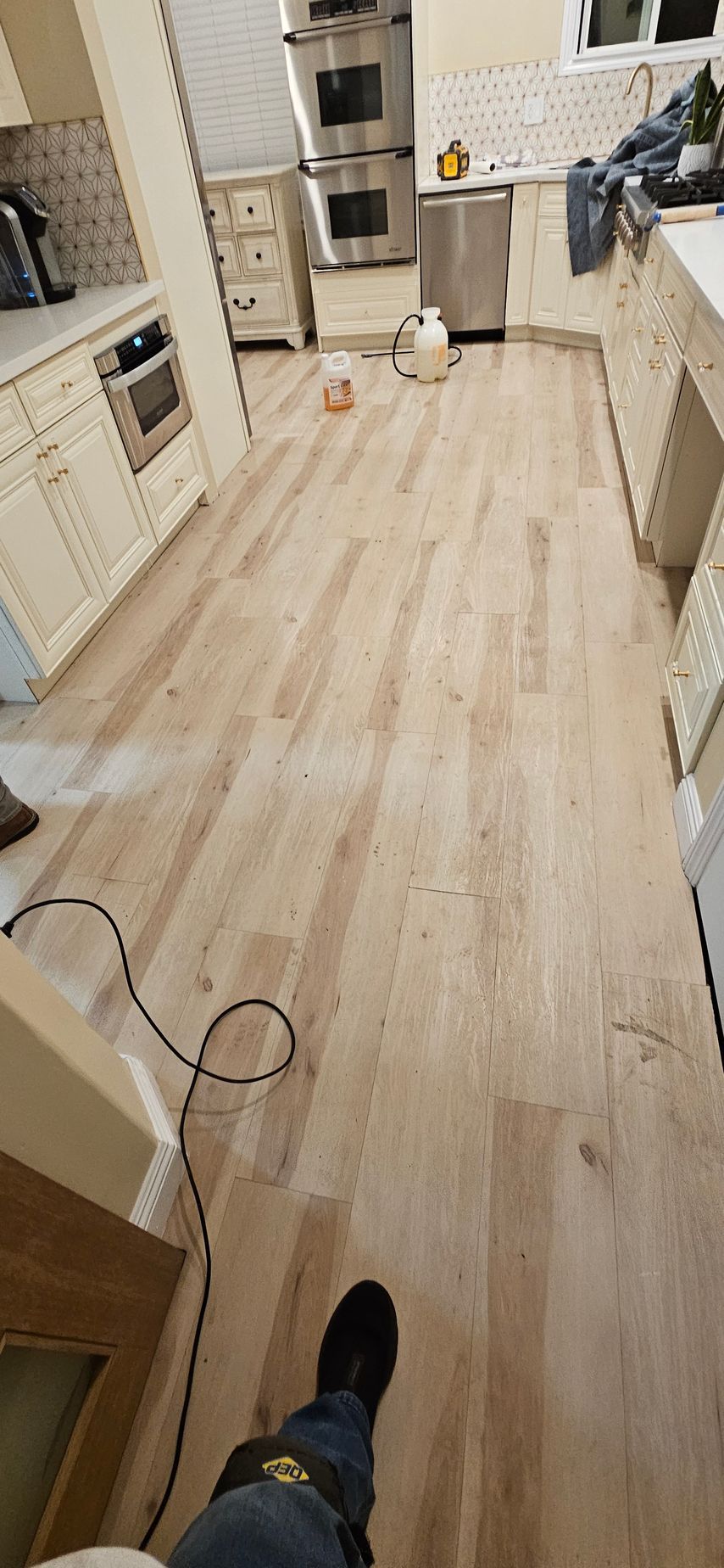 A person is standing on a wooden floor in a kitchen.