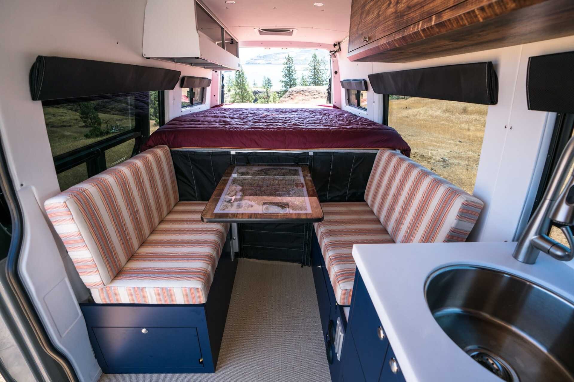 The inside of a van with a bed , couch , table and sink.