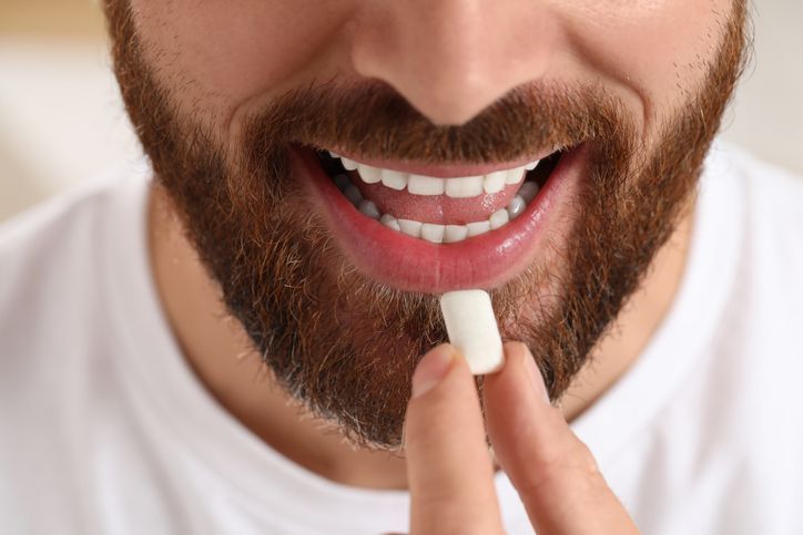 A close-up of a person with a beard putting a white pill into their mouth.