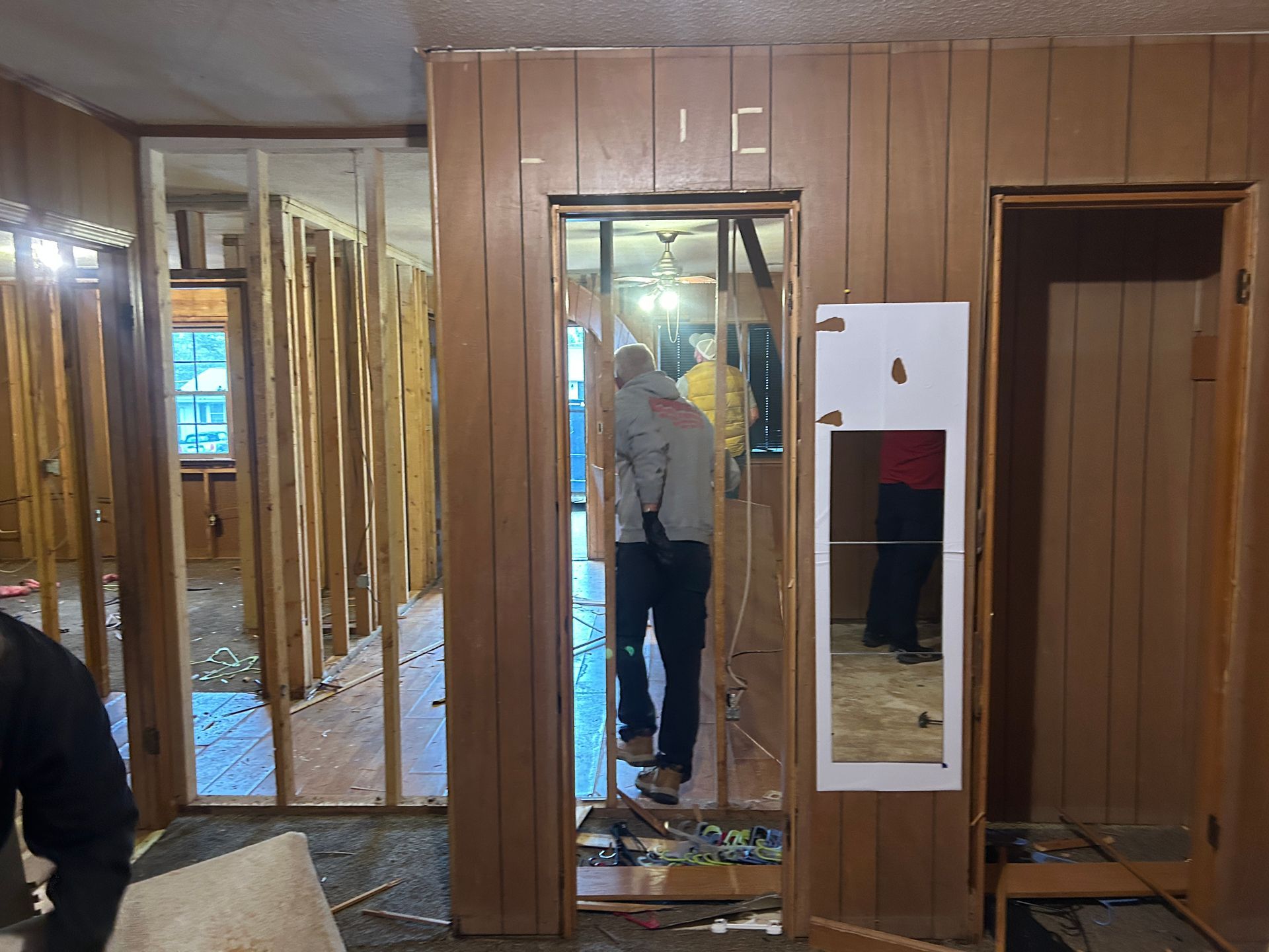 A man is standing in a room with wood paneling and a mirror.
