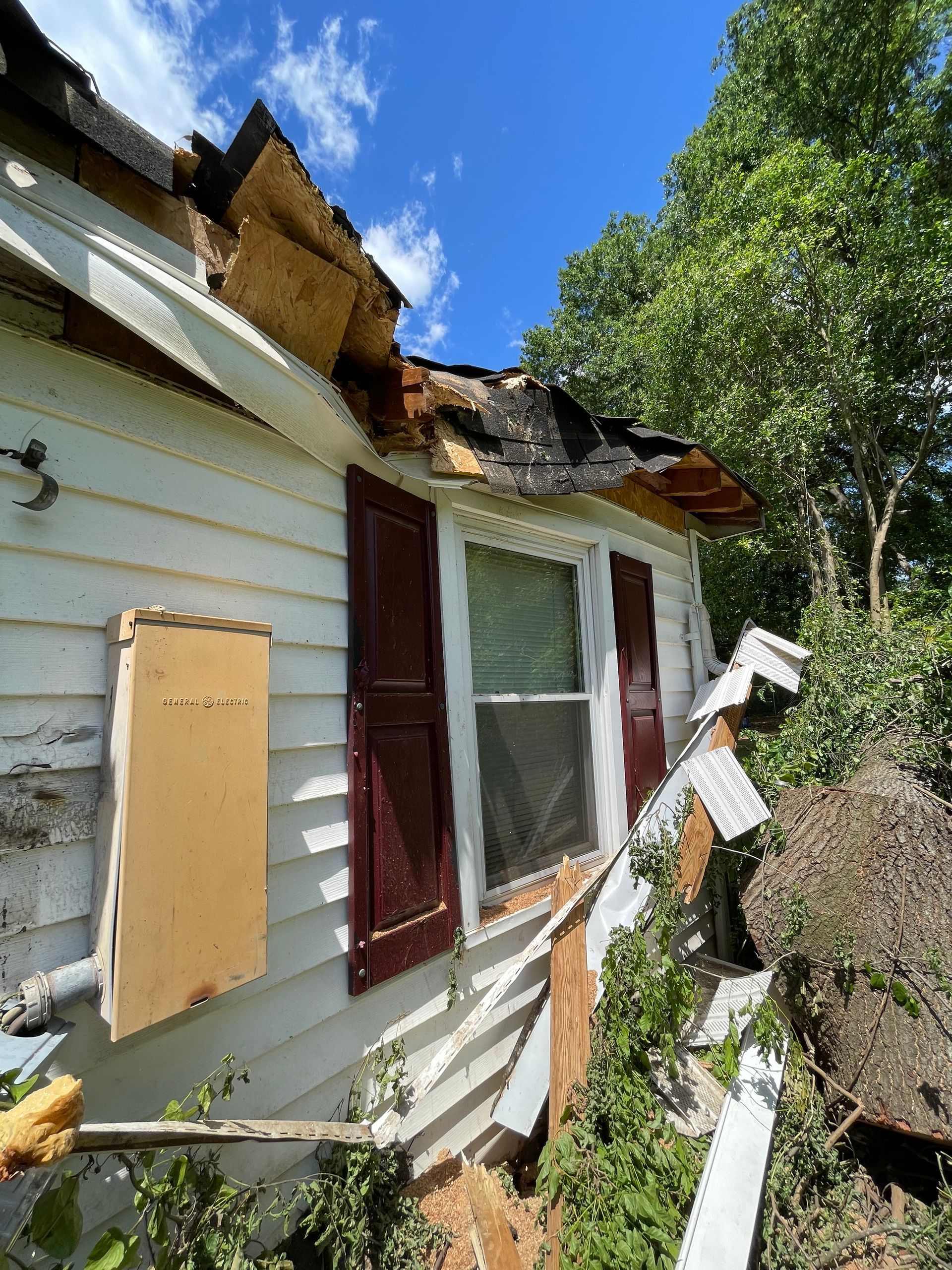 A white house with a roof that has been damaged by a storm.