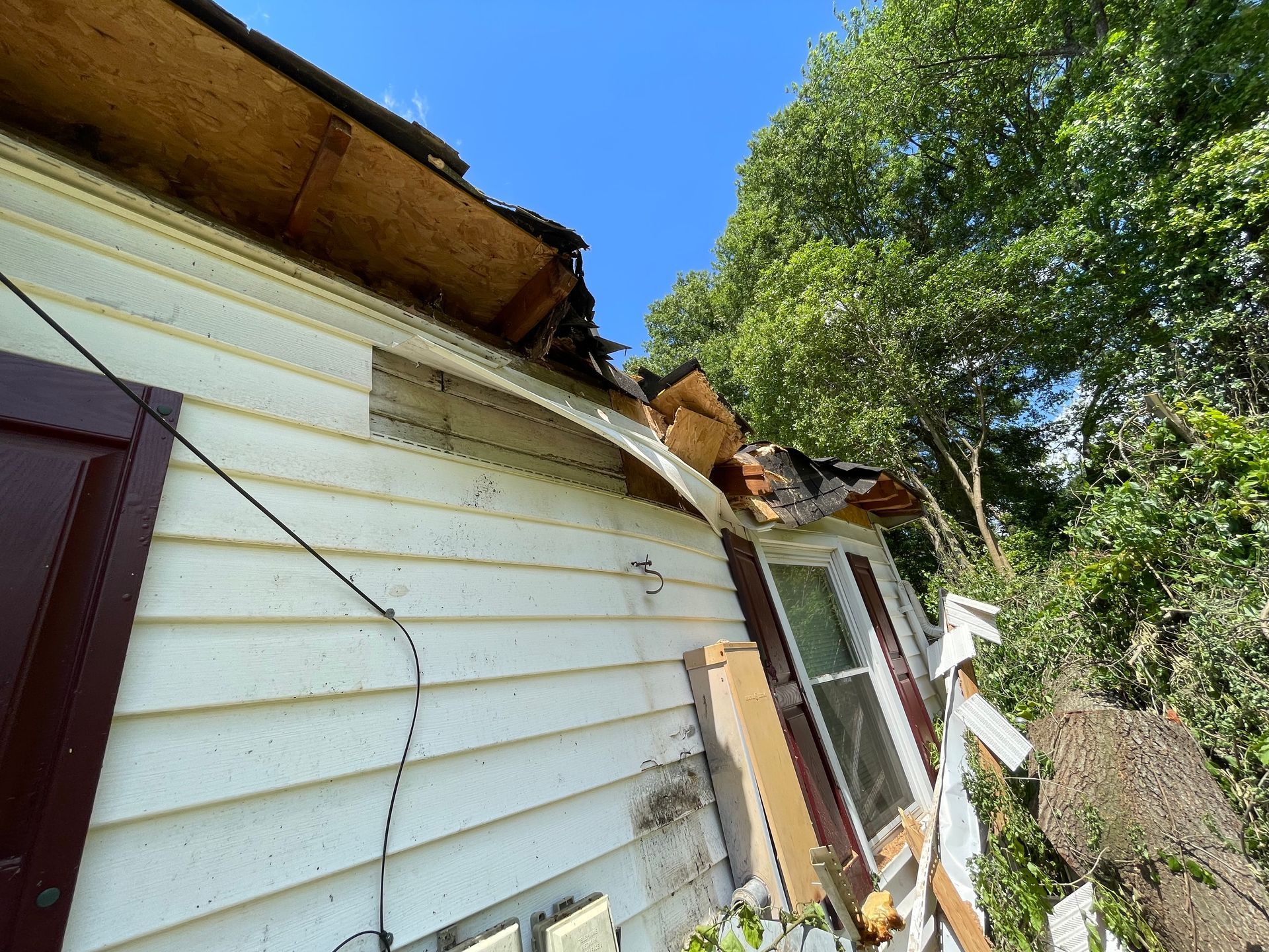 A white house with a roof that has been damaged by a storm.