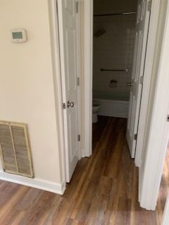 A hallway with hardwood floors leading to a bathroom and a toilet.