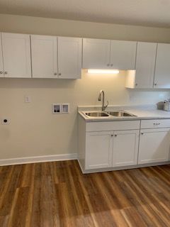 A kitchen with white cabinets , a sink , and hardwood floors.
