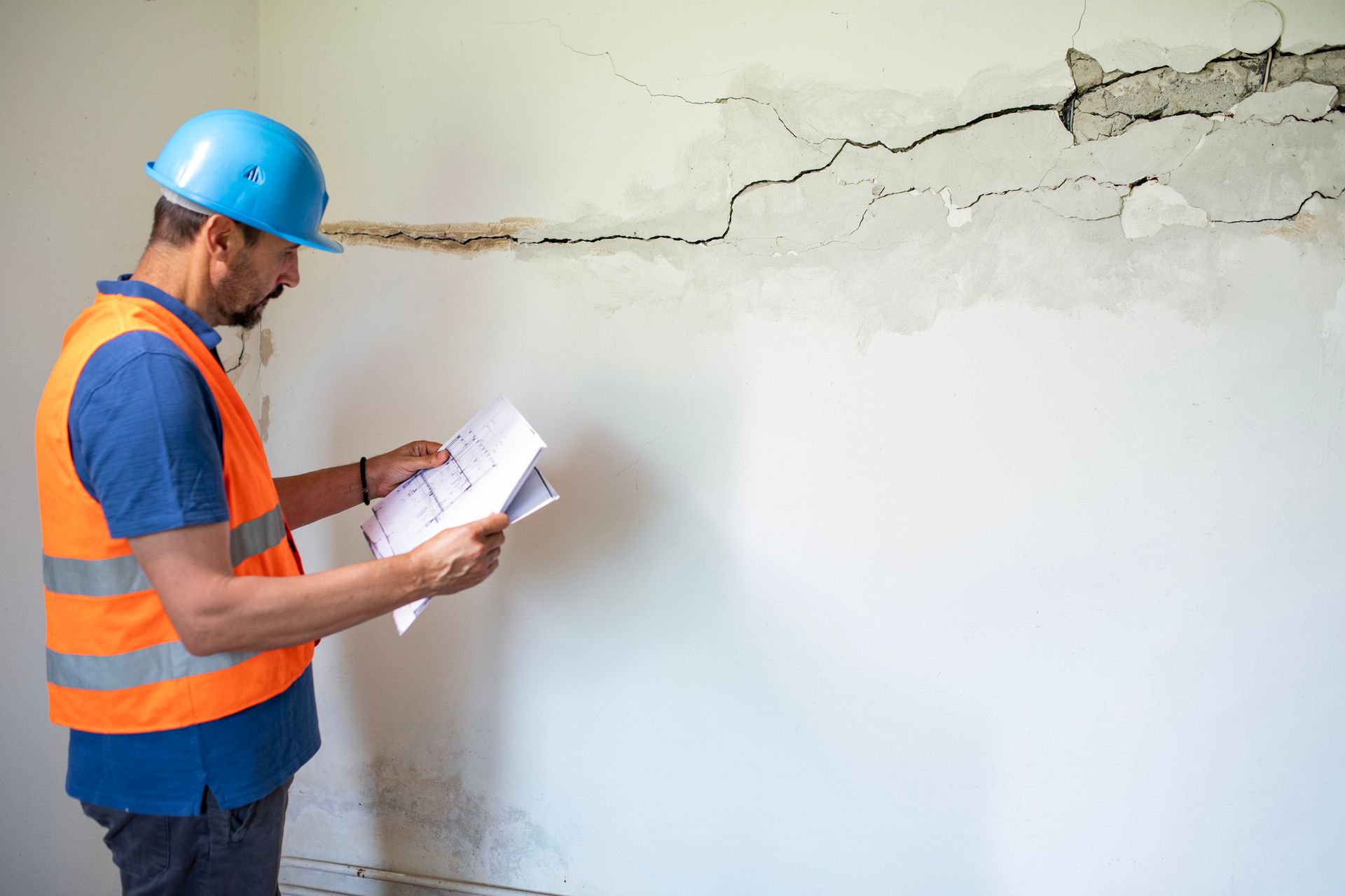 A man stands beside a cracked, damp wall, recognizing the urgent need for water damage cleanup.