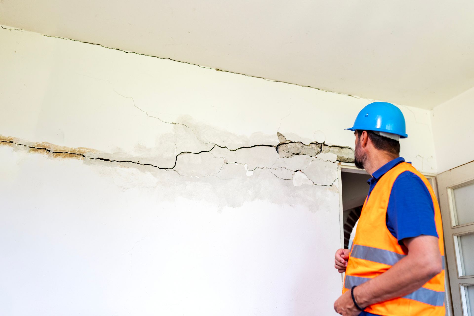 A man in orange vest examines cracked wall for water damage cleanup service.