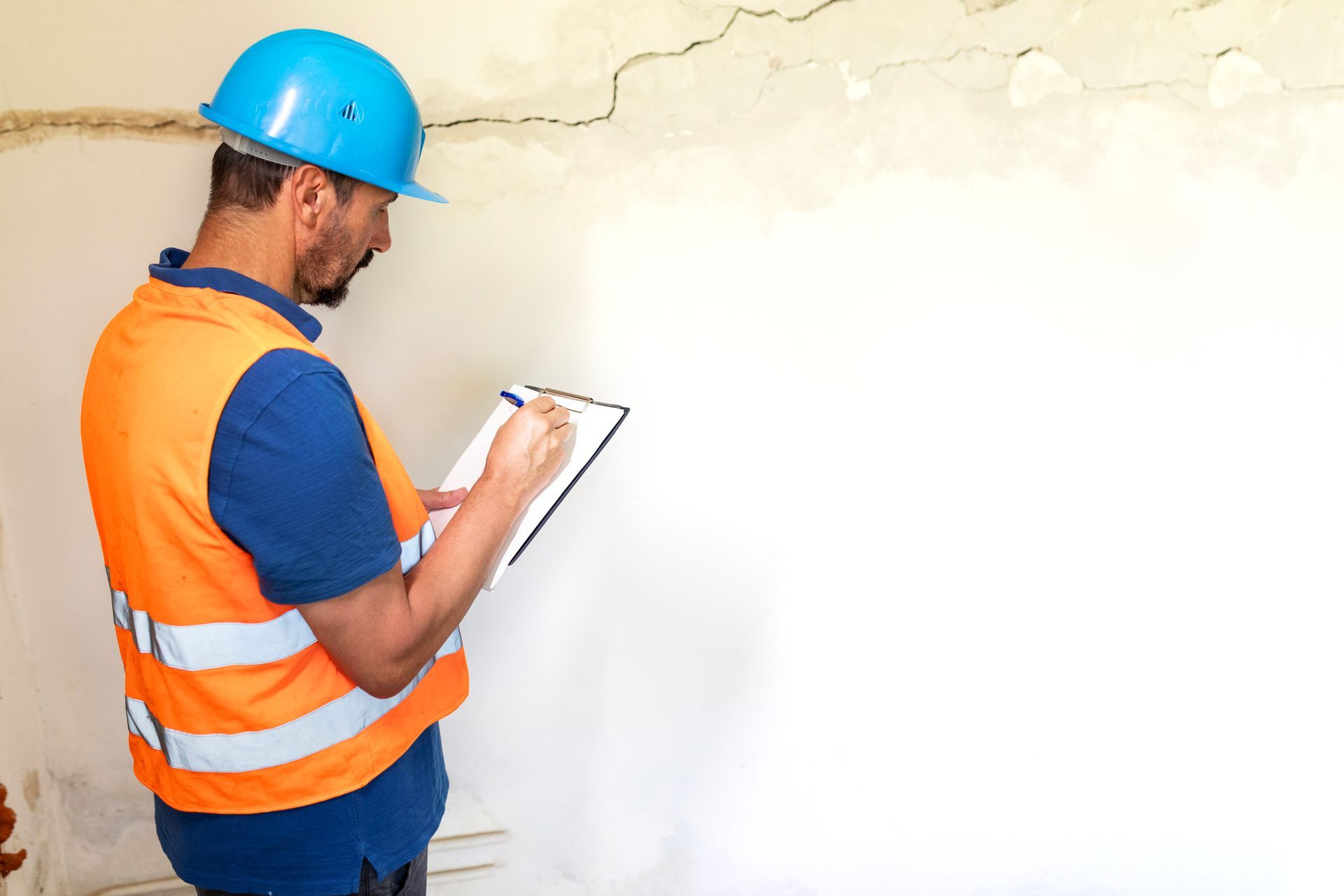 A man stands by a cracked wall, noticing the need for a water damage cleanup Service.