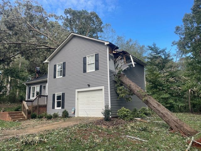 A house with a tree fallen on it in front of it.