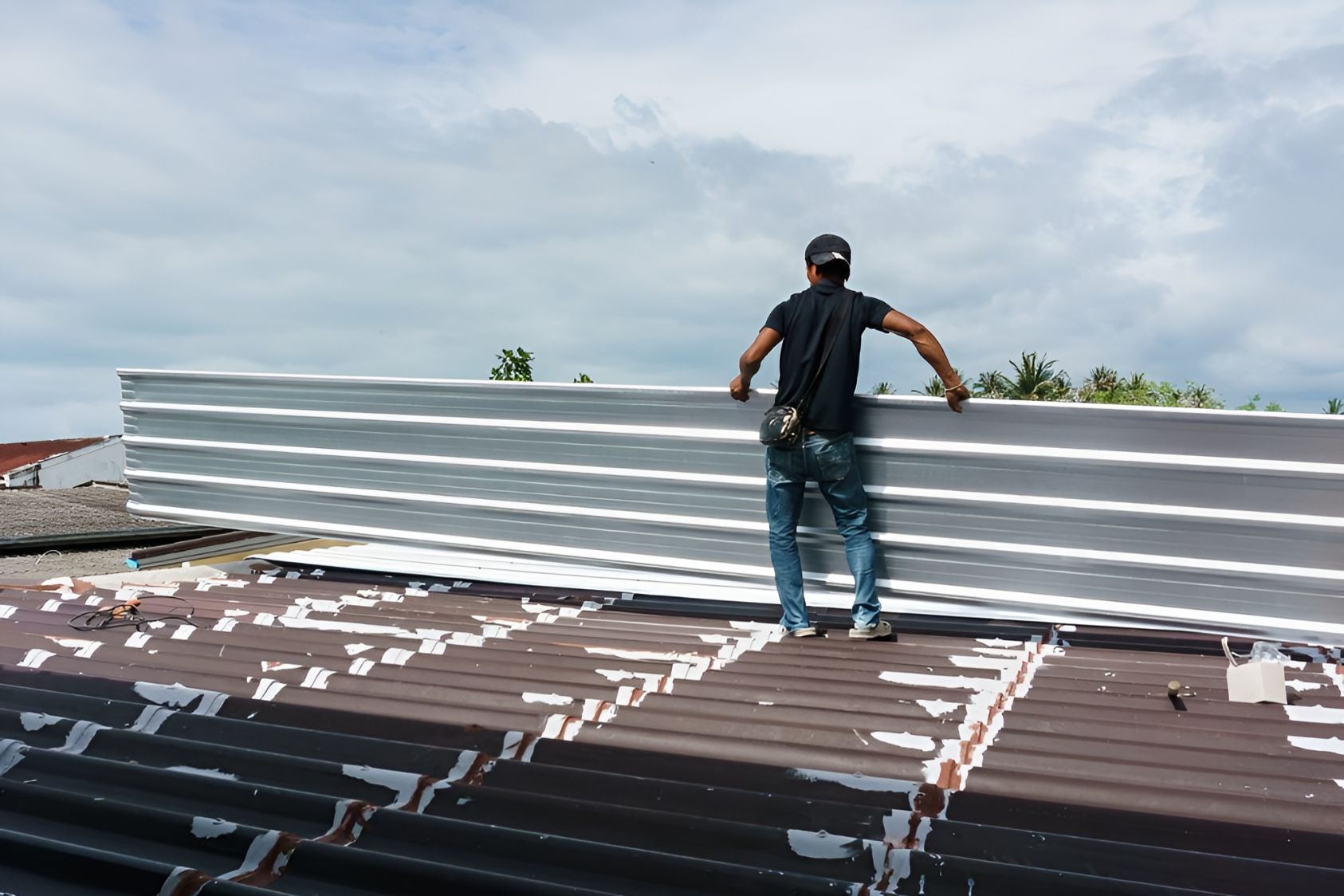 A Man is Standing on Top of a Roof Holding a Piece of Metal — Goonellabah Roof Tilers in Bangalow, NSW