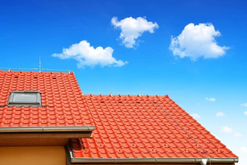 Red-Tiled House Roof with A Skylight Under a Bright Blue Sky and Clouds — Goonellabah Roof Tilers In Northern Rivers, NSW