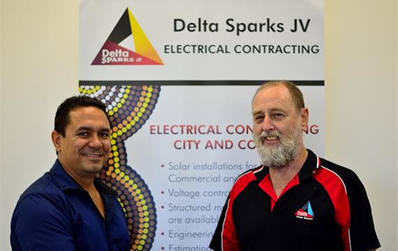 two men stand in front of a delta sparks jv electrical contracting sign