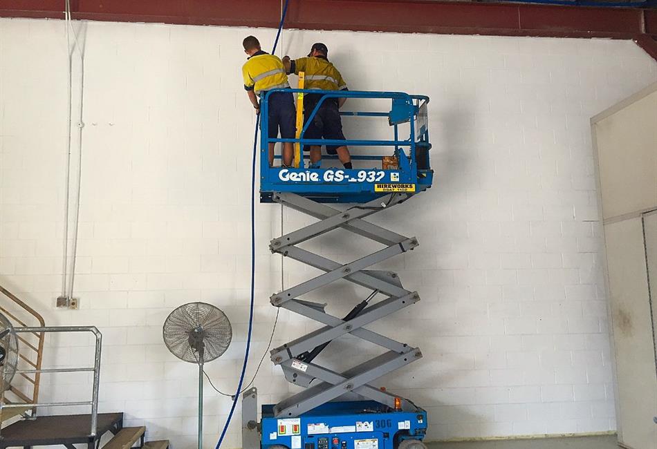 two men are working on a genie scissor lift in a warehouse .