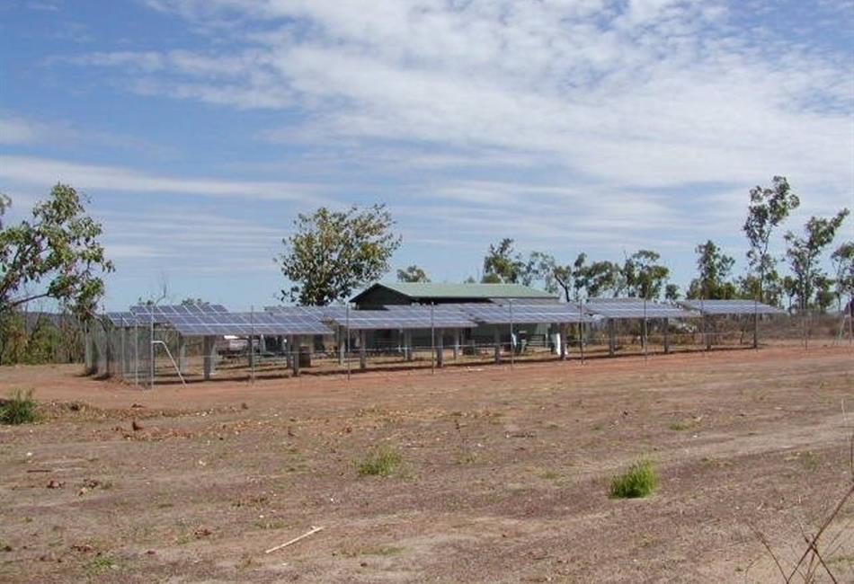 a row of solar panels in a field with a house in the background