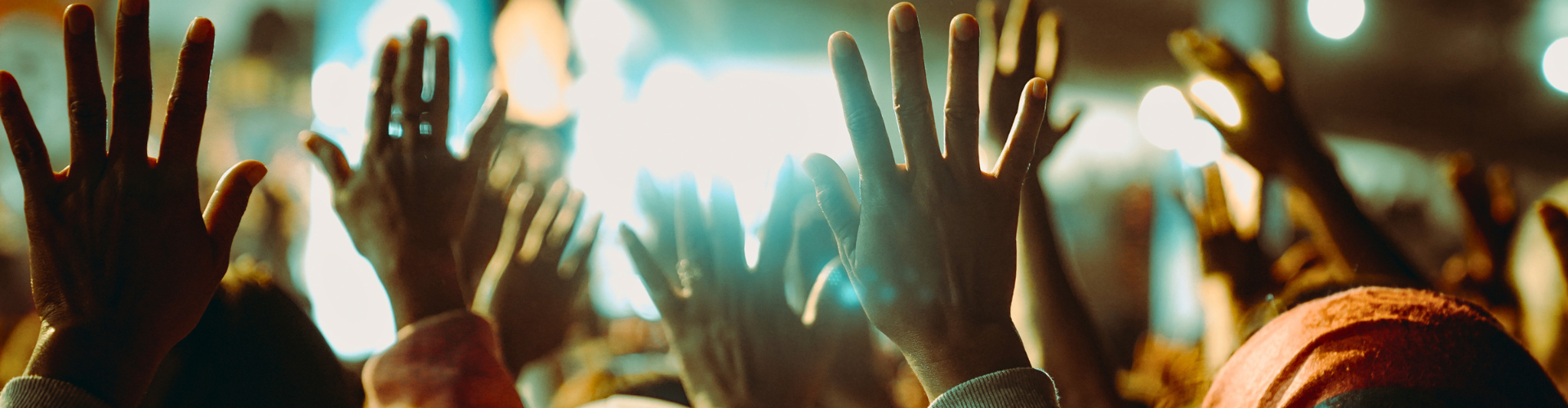 Crowd with raised hands at a concert, bright stage lights glowing in the background
