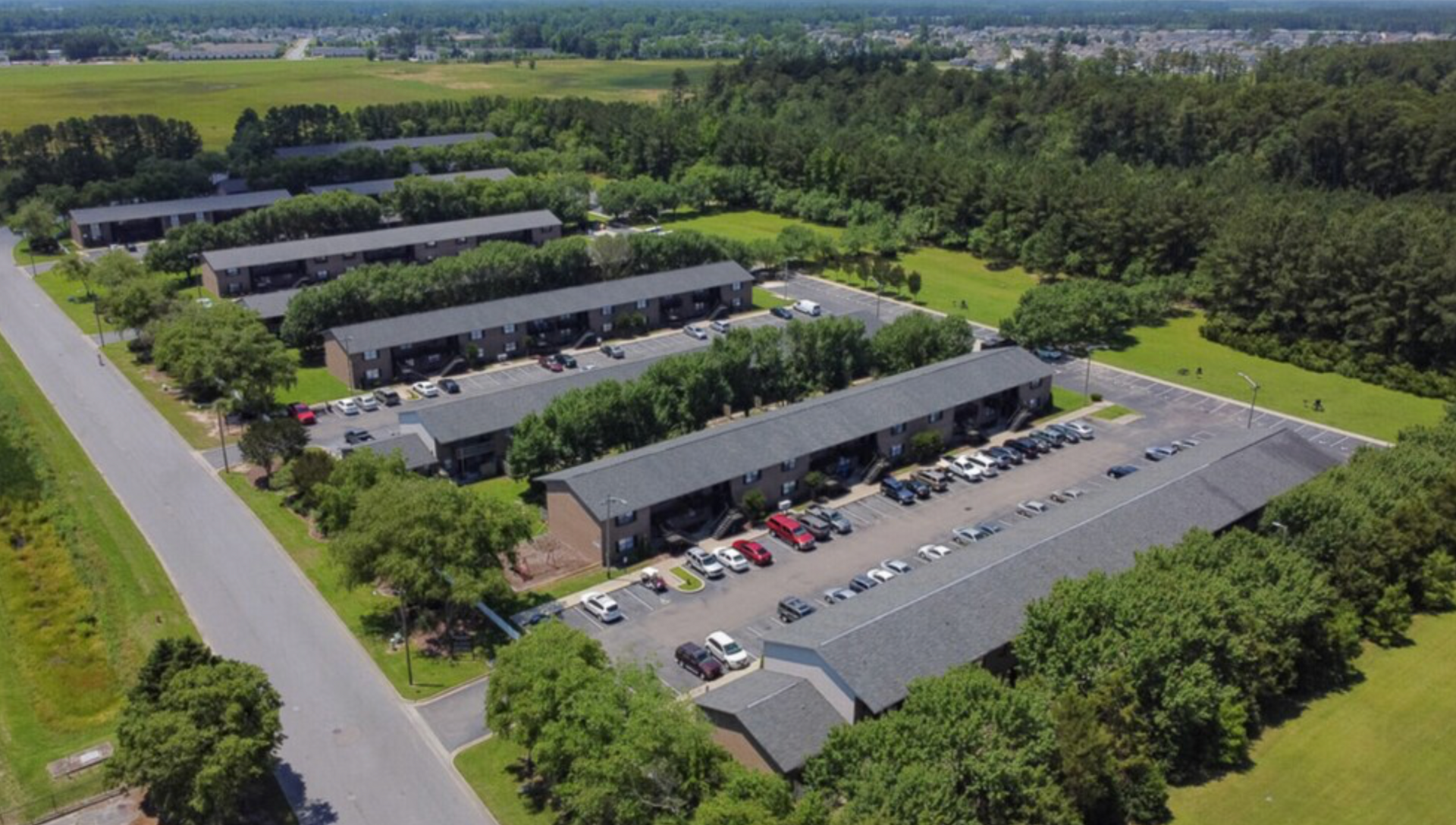 An aerial view of a row of apartment buildings surrounded by trees and a parking lot.