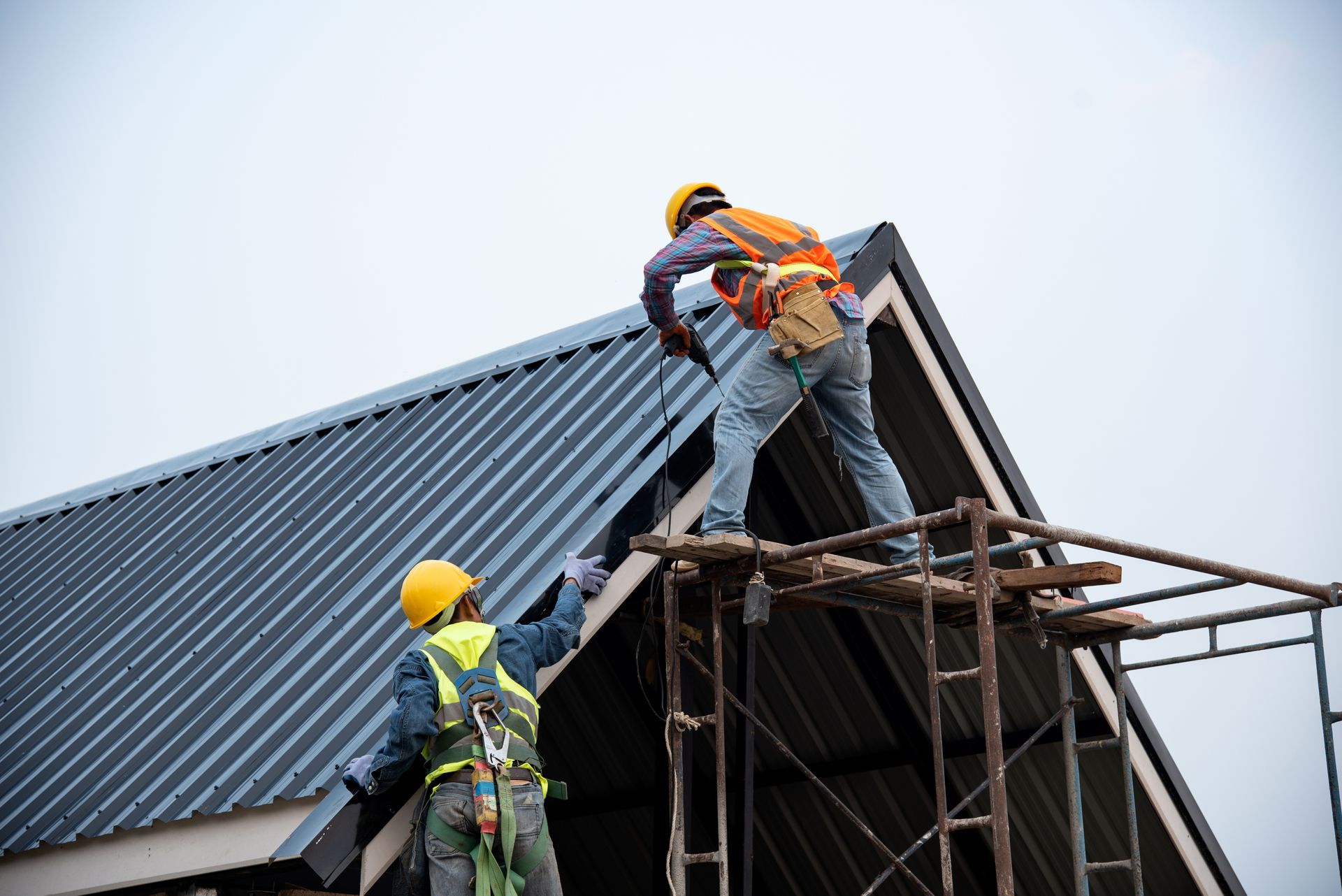 A worker on a ladder installs green foam exterior insulation board onto the side of a house.