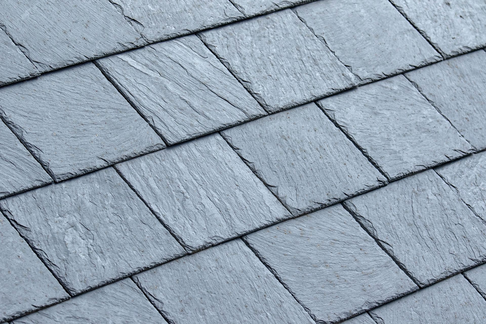 A person's hands positioning a dark brown asphalt shingle onto an underlayment-covered roof during installation.