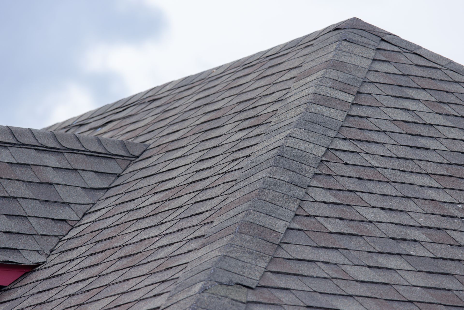 A sloped, shingled roof covered in light frost with a metal vent and a brick chimney under a cloudy sky.