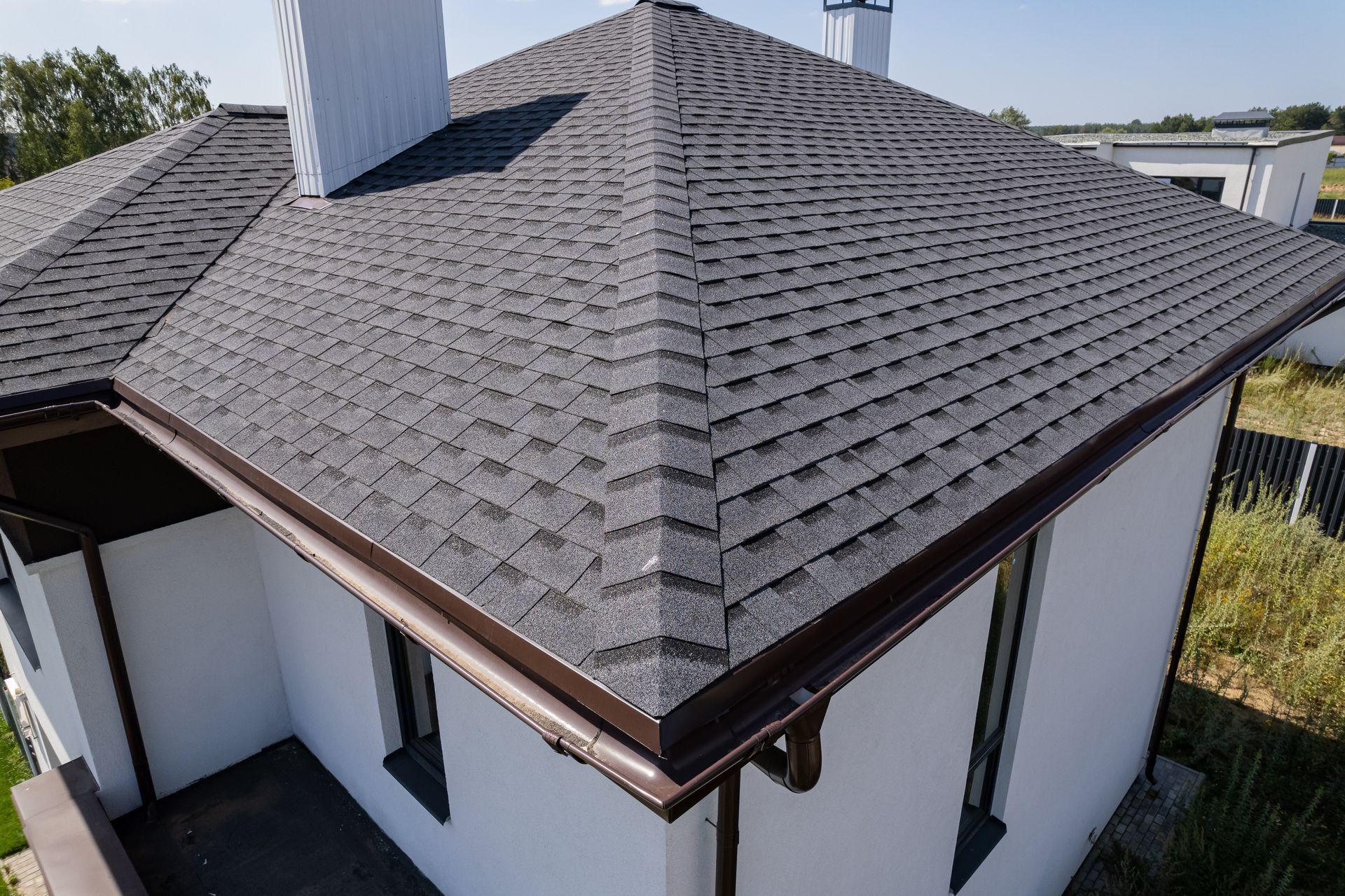 Aerial view of a house with a gray shingled hip roof and white exterior walls.