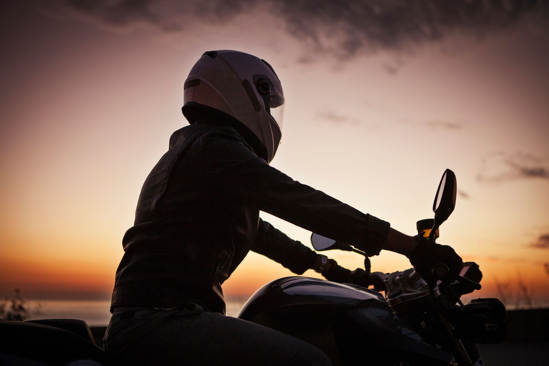 A person wearing a helmet is riding a motorcycle at sunset.