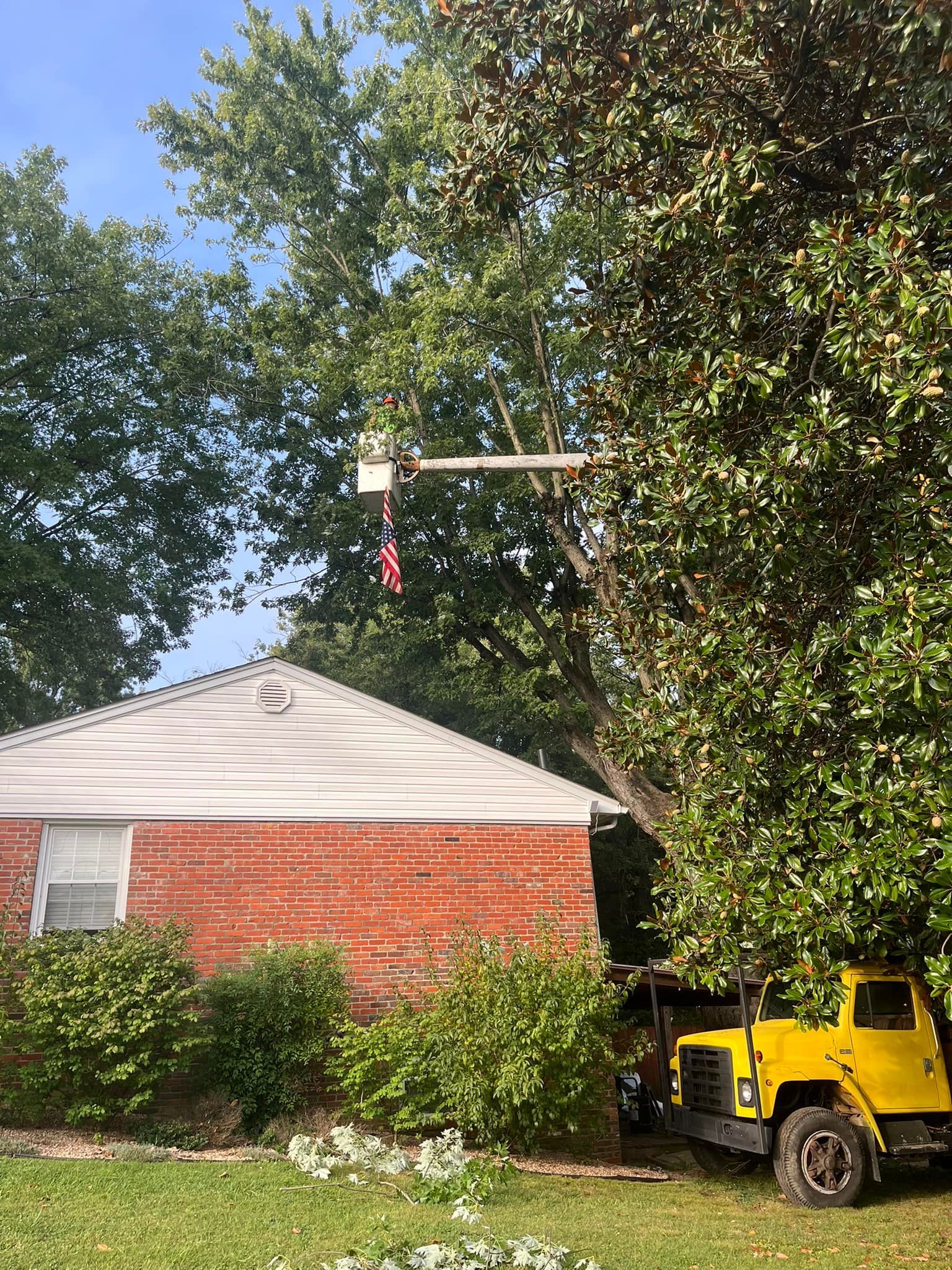 a yellow truck is cutting a tree in front of a brick house .