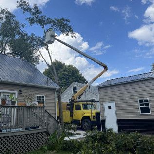 a yellow truck is cutting a tree in front of a house .