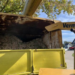 a yellow dumpster is being filled with wood chips .