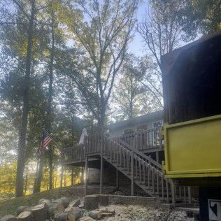 a house with a deck and stairs is surrounded by trees .